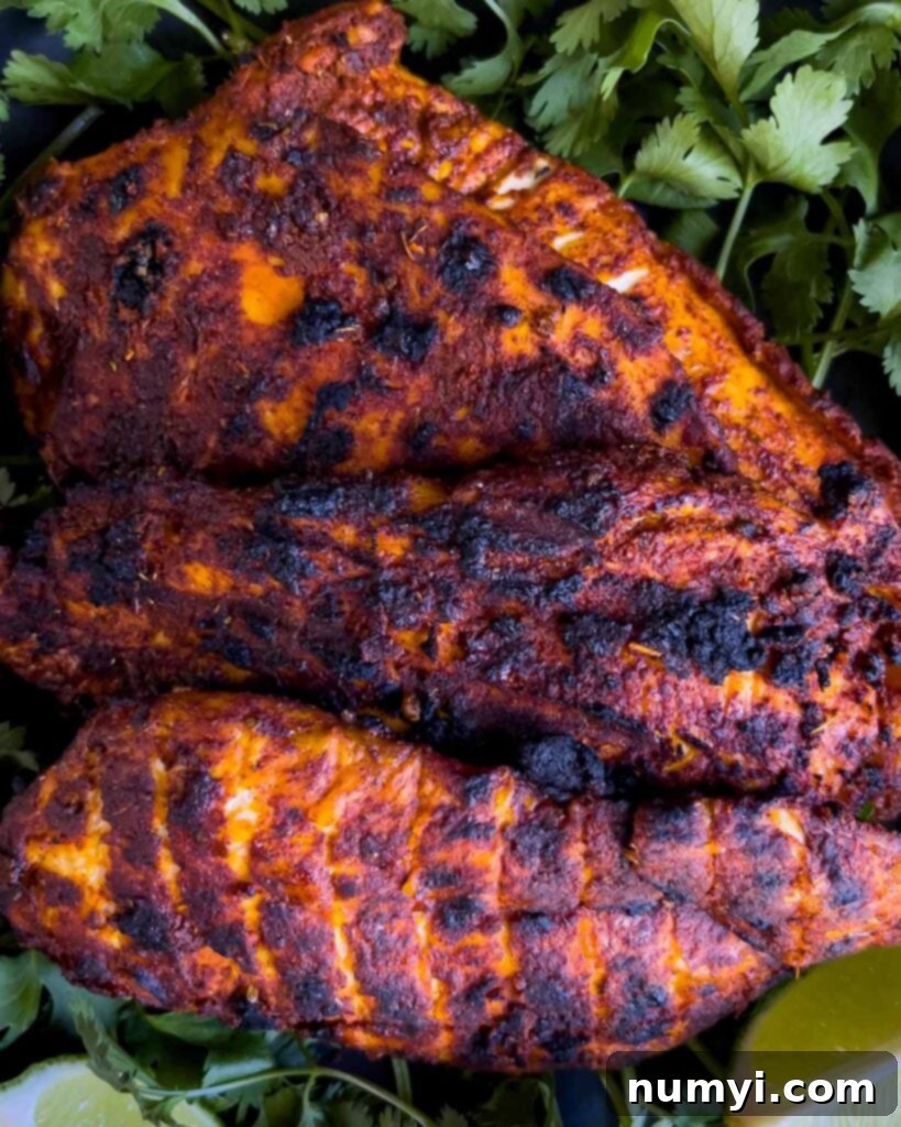 Close-up of perfectly grilled Mexican chicken breast (Pechuga Asada) on a bed of fresh cilantro, highlighting its delicious char.