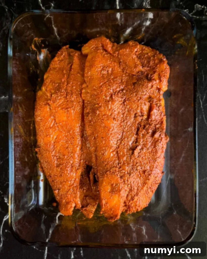 Chicken breasts fully coated in a rich, reddish-orange annatto-based marinade, ready for grilling.