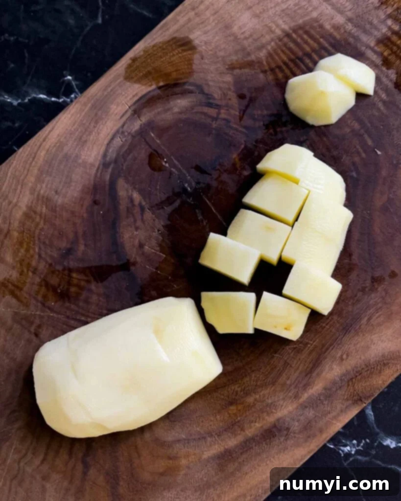 Russet potato diced into uniform 1-inch pieces on a wooden cutting board, ready for boiling.