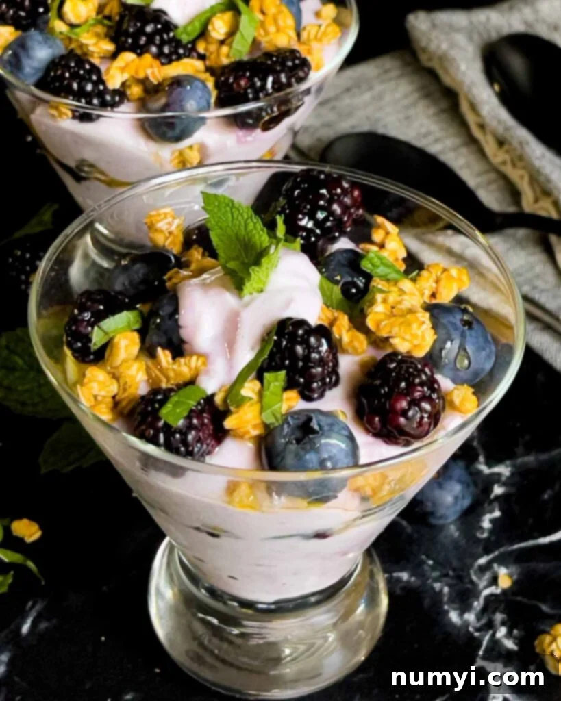 Refreshing Berry Yogurt Parfait 3 Berry yogurt parfait in a stemless martini glass on a dark surface.
