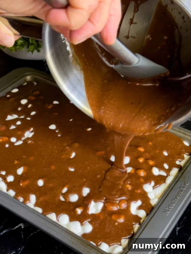 The Easiest Mississippi Mud Cake 13 Chocolate frosting being poured over the melted mini marshmallows on the Mississippi Mud Cake.