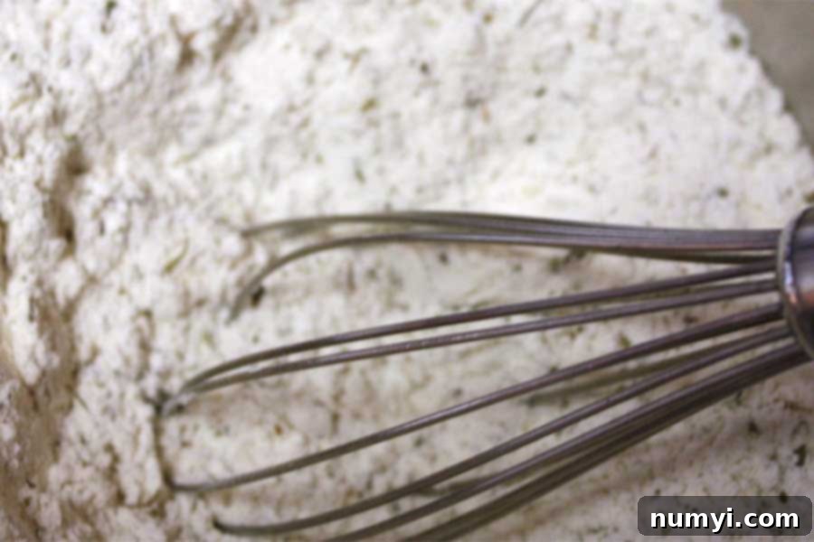 Dry ingredients, including flour and Herbes de Provence, whisked together in a mixing bowl.