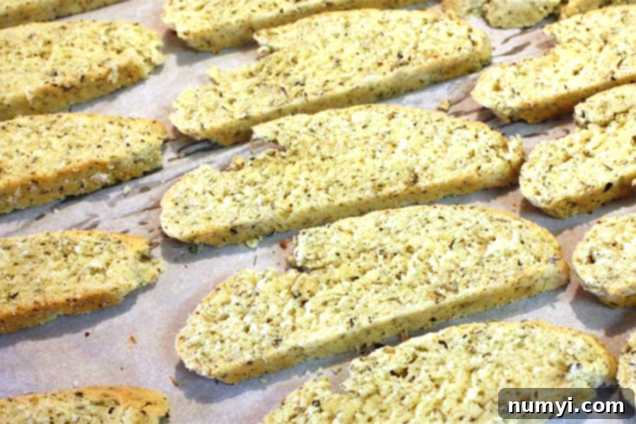 Sliced savory herb and cheese biscotti arranged cut-side down on a parchment-lined baking sheet, ready for the second bake.