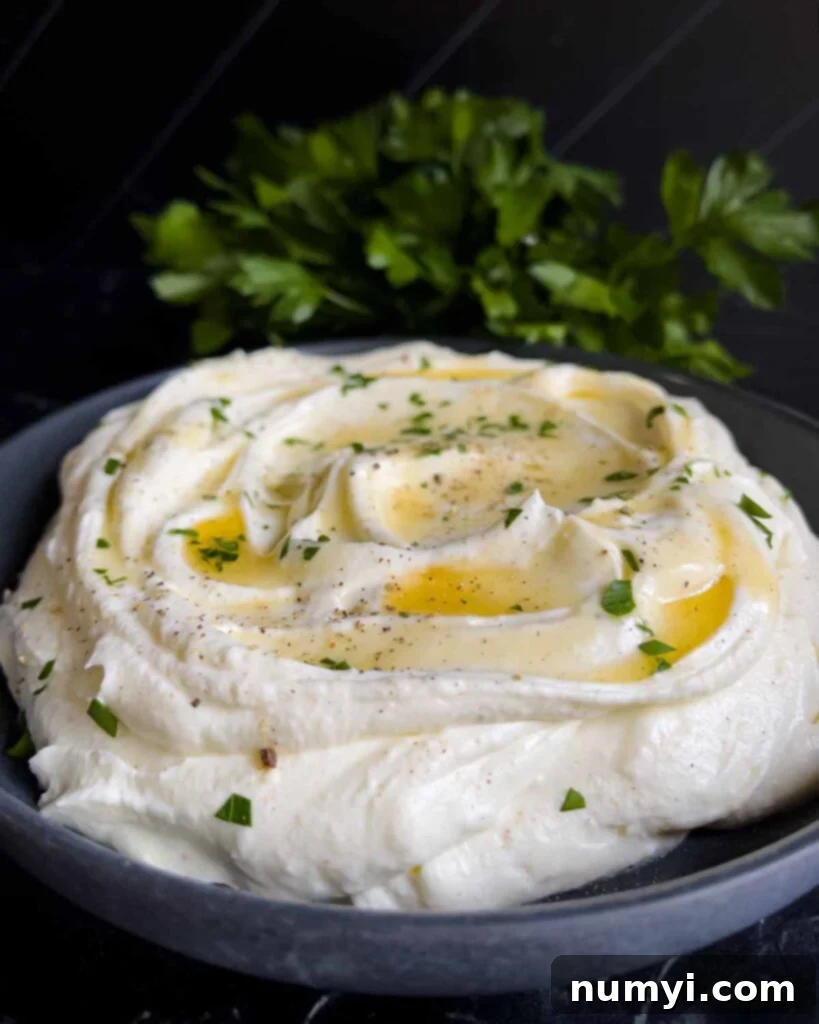 Whipped feta garnished with honey, chopped parsley, and black pepper in a dark bowl.