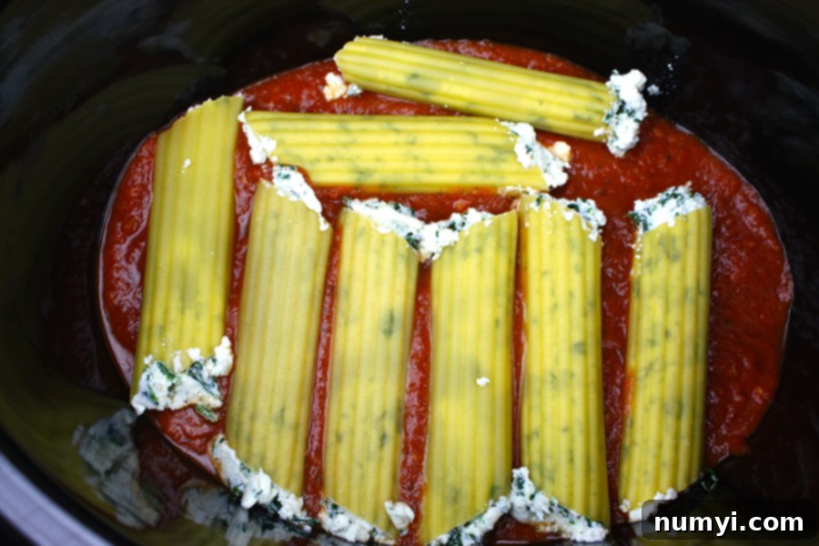Spinach Ricotta Manicotti shells arranged on a bed of marinara sauce in the crock of a slow cooker.