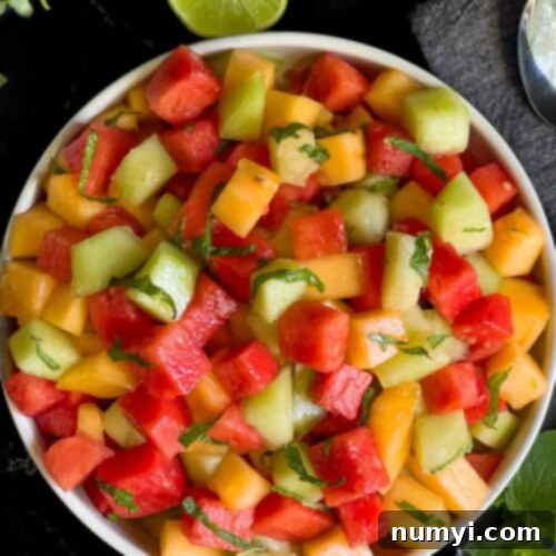 Mixed Melon Fruit Salad with Honey Lime and Mint 11 Mixed melon fruit salad in a white bowl on a dark surface.