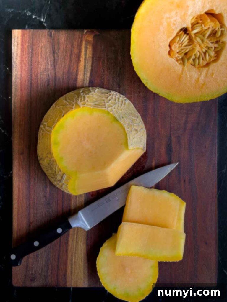 Mixed Melon Fruit Salad with Honey Lime and Mint 4 A cantaloupe cut in half with its skin meticulously removed, placed on a dark wooden cutting board, showcasing the vibrant orange flesh.