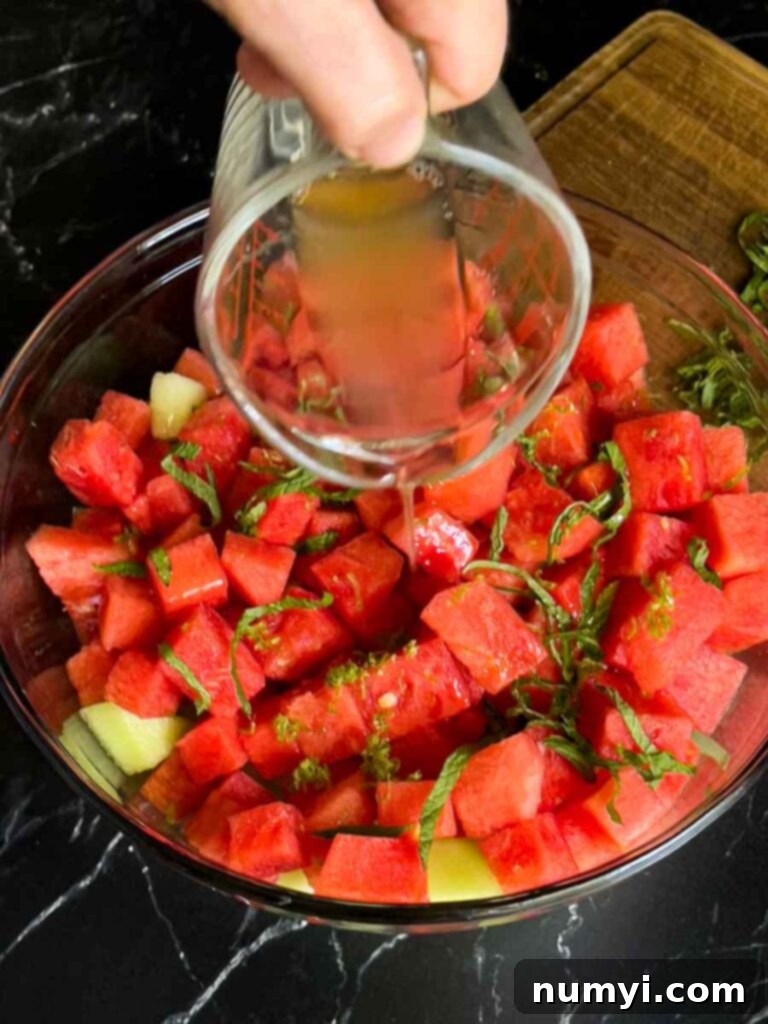 Mixed Melon Fruit Salad with Honey Lime and Mint 8 The luscious honey-lime dressing being carefully poured over the colorful mixed melon fruit salad in a glass bowl.