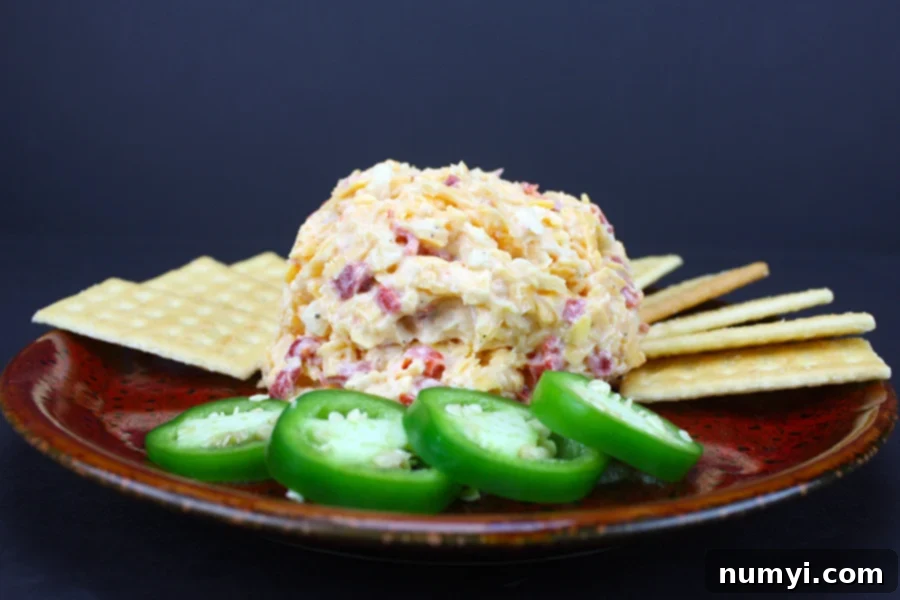 A close-up of homemade pimento cheese artfully arranged on a red plate, surrounded by an assortment of crackers and vibrant jalapeño slices.