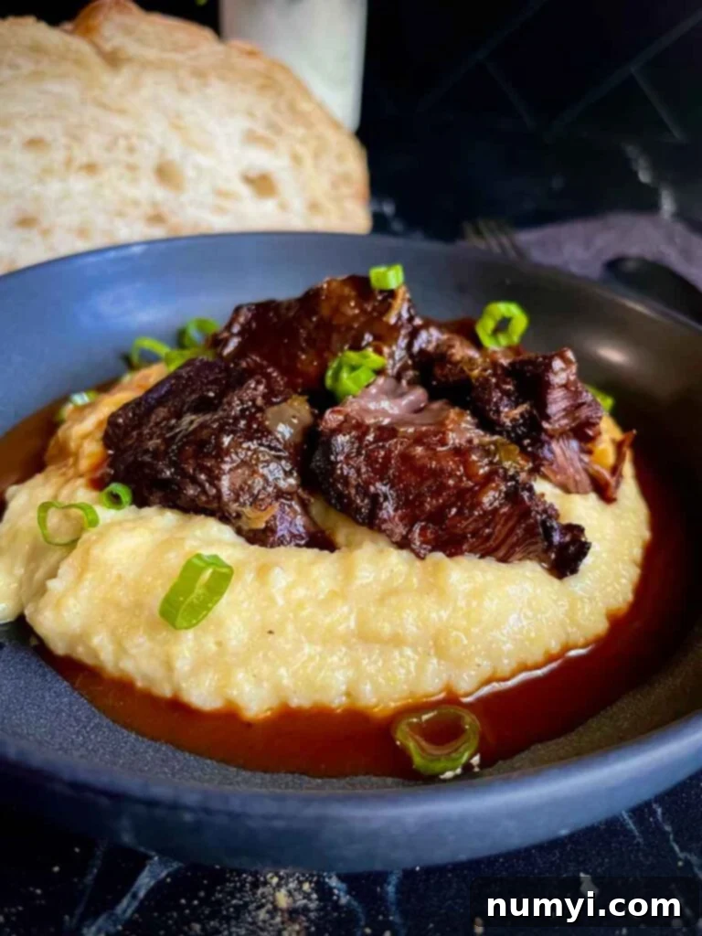 A plated dish of braised beef cheek on creamy polenta, garnished with fresh green onion, showcasing the finished recipe.