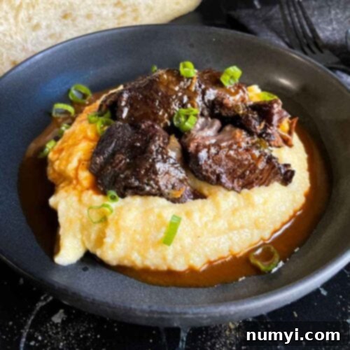 Braised beef cheek on a bed of polenta, garnished with fresh green onion.