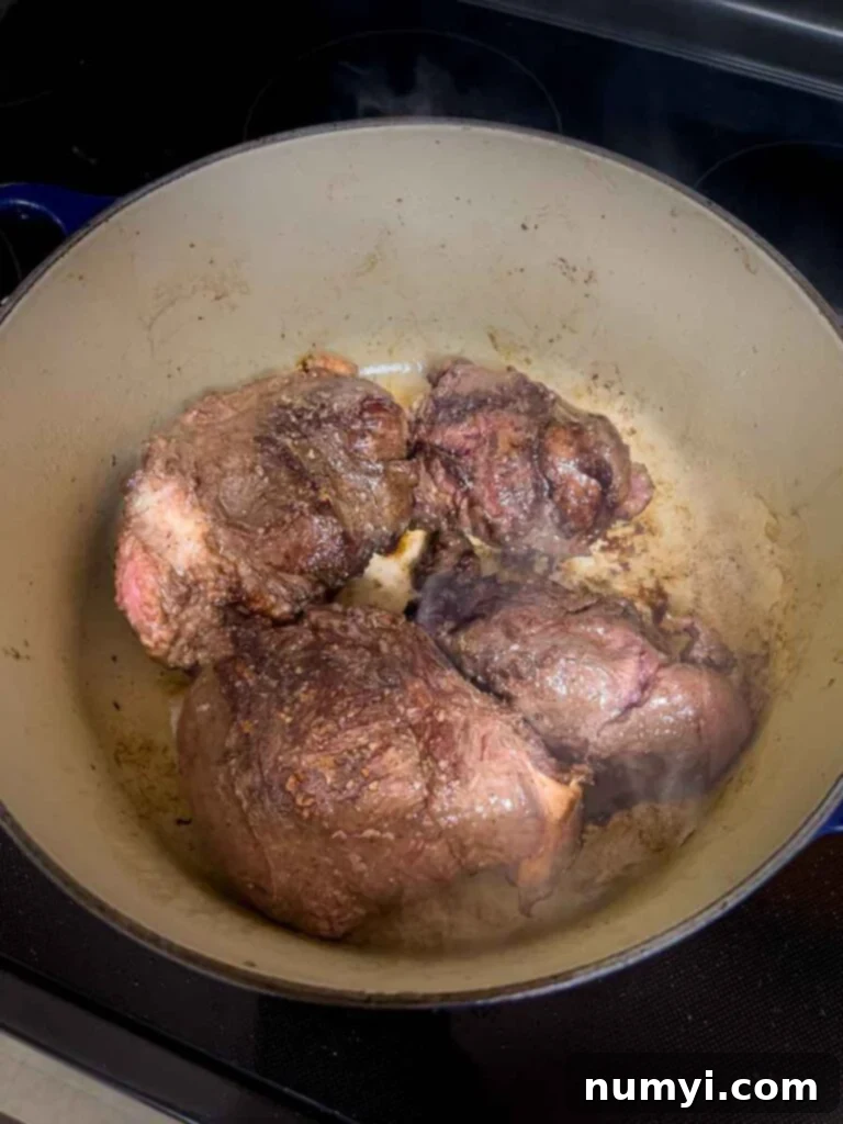 A piece of beef cheek being seared in a hot Dutch oven with olive oil, developing a rich brown crust.