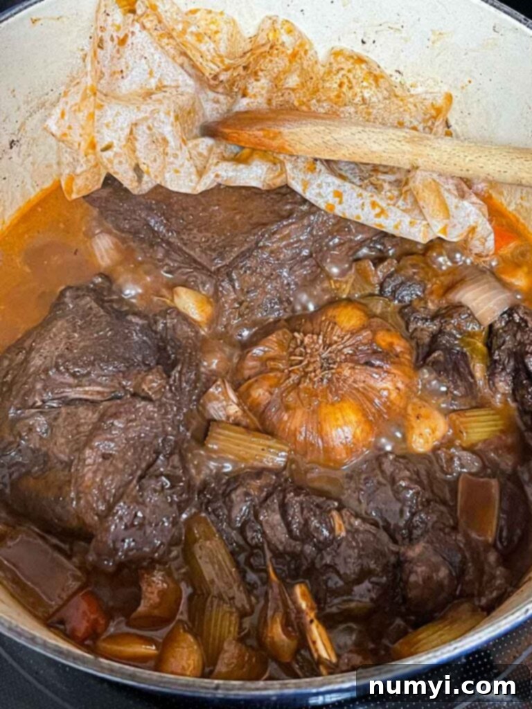 Braised beef cheeks simmering in a Dutch oven, covered with a lid, illustrating the slow-cooking process.
