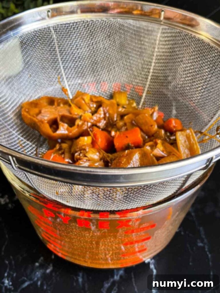The braising liquid being strained through a sieve to remove cooked vegetables and create a smooth gravy.