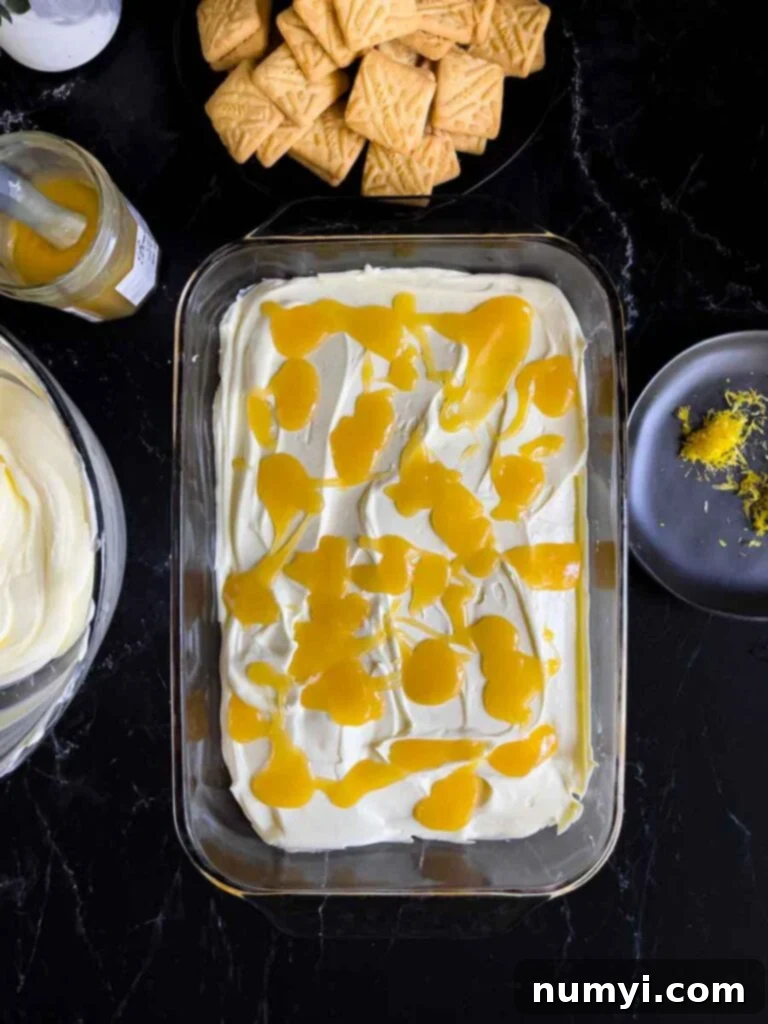 First layer of the lemon icebox cake completed in a glass baking dish on a dark surface.