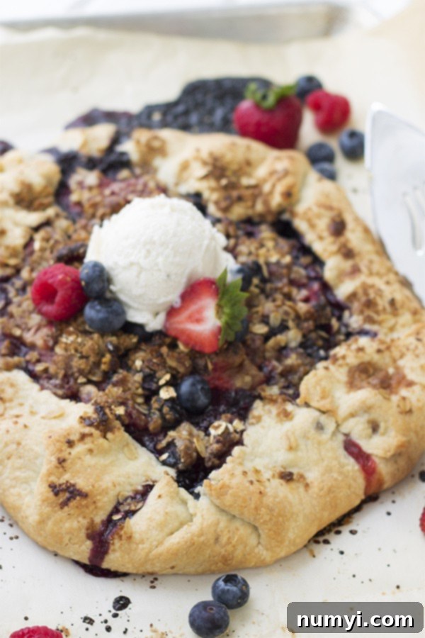 A freshly baked berry galette cooling on a baking sheet, topped with a scoop of creamy vanilla ice cream and surrounded by fresh, vibrant mixed berries.