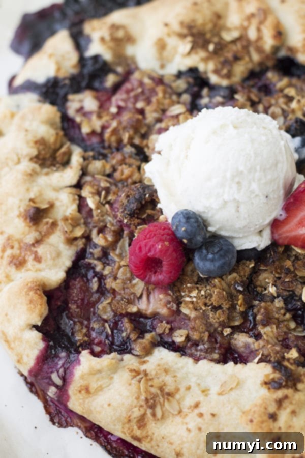 A close-up photograph of a vibrant berry galette, overflowing with juicy mixed berries and generously topped with a dollop of creamy vanilla ice cream, showcasing the rich textures and colors.