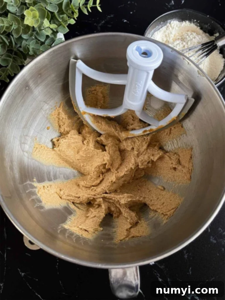 Creamy peanut butter and unsalted butter being beaten together in a metal mixing bowl.