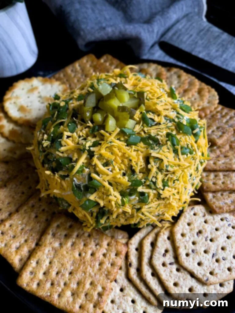 Dill pickle cheese ball on a dark plate on a dark surface with grey napkins.