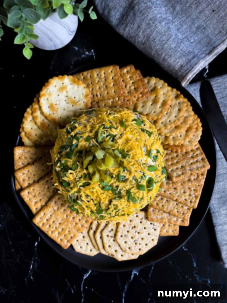 Dill pickle cheese ball on a dark plate on a dark surface with grey napkins.
