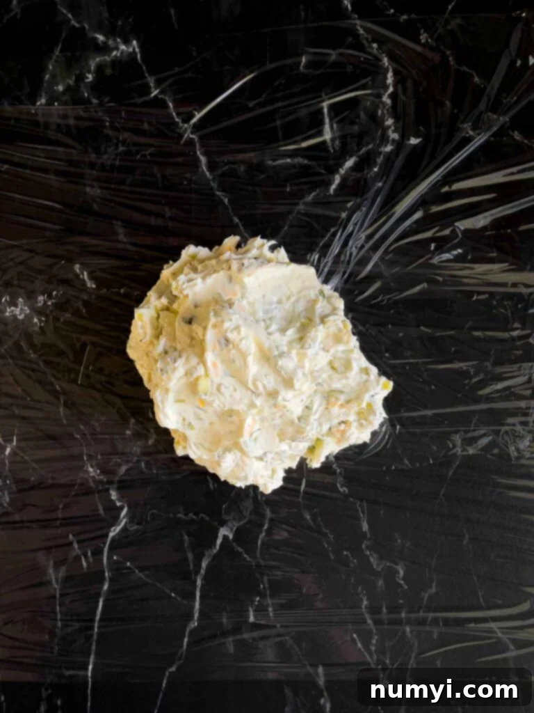 Dill pickle cheese ball ingredients mixed together and placed on plastic wrap on a dark surface.