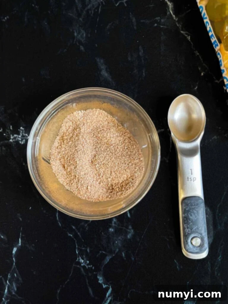 Cinnamon sugar topping for oyster cracker churro snack mix in a glass ramekin on a dark surface.