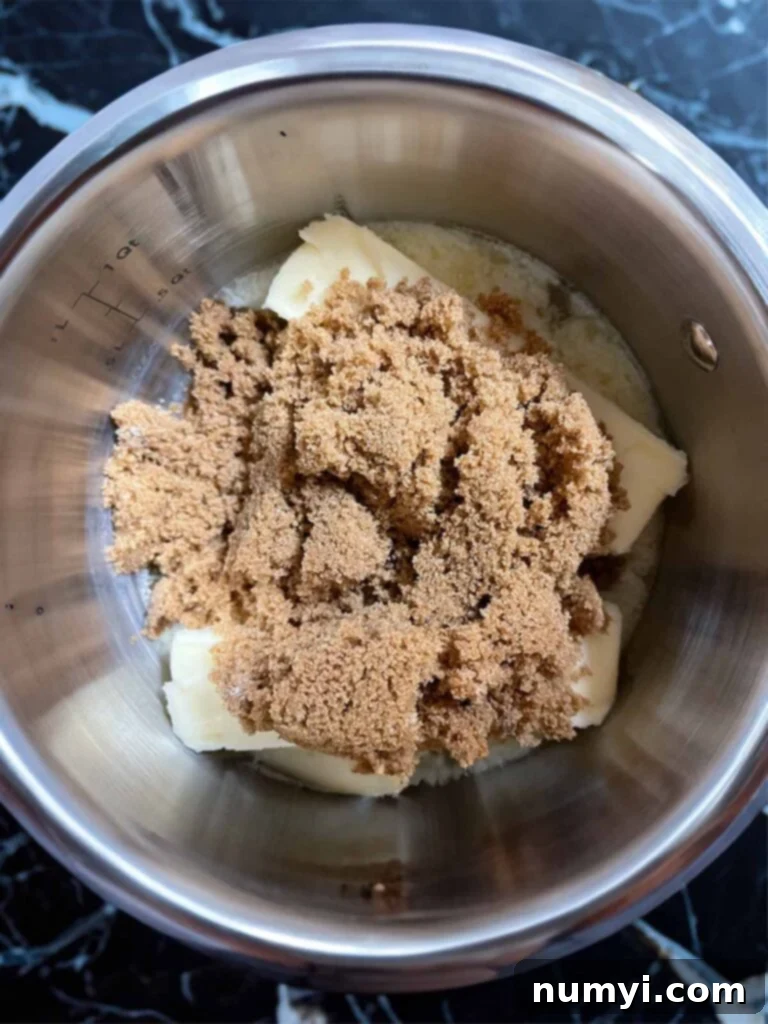 Dark brown sugar and butter for oyster cracker churro snack mix in a silver saucepan on a dark surface.
