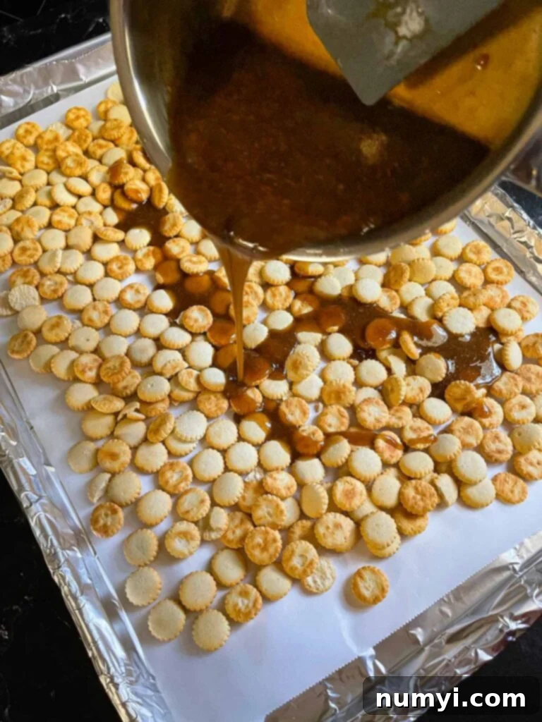Pouring the toffee mixture over the oyster crackers in a lined baking sheet.