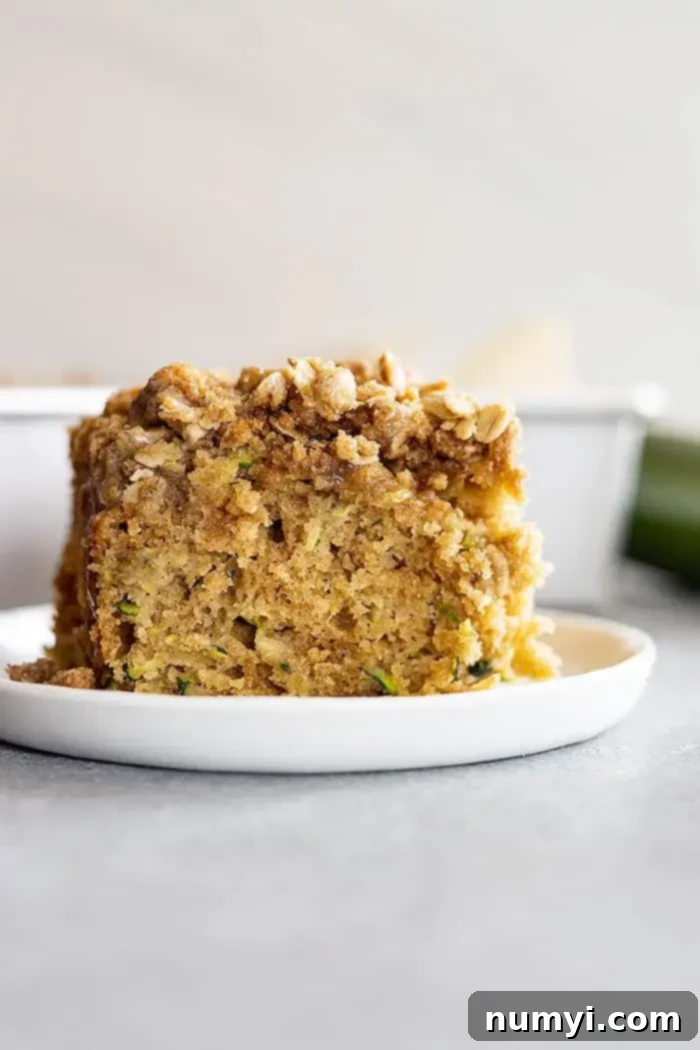 A large serving of moist zucchini cake with a generous streusel topping, viewed from the side, ready to be enjoyed.