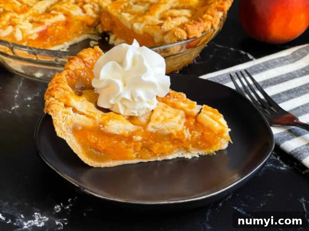 A beautifully presented slice of Southern peach pie topped with a dollop of whipped cream on a dark plate, showcasing the golden lattice crust and juicy filling.