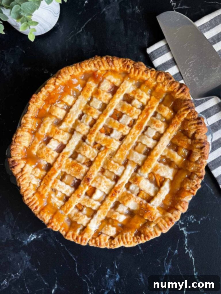 A freshly baked peach pie with a golden-brown lattice crust, cooling on a wire rack with a striped napkin and pie slicer in the background.