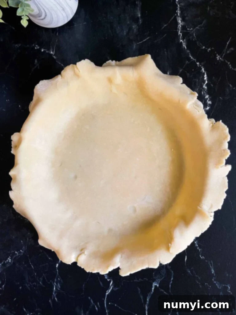 A raw, unbaked pie crust expertly fitted into a ceramic pie baking dish, ready for filling.