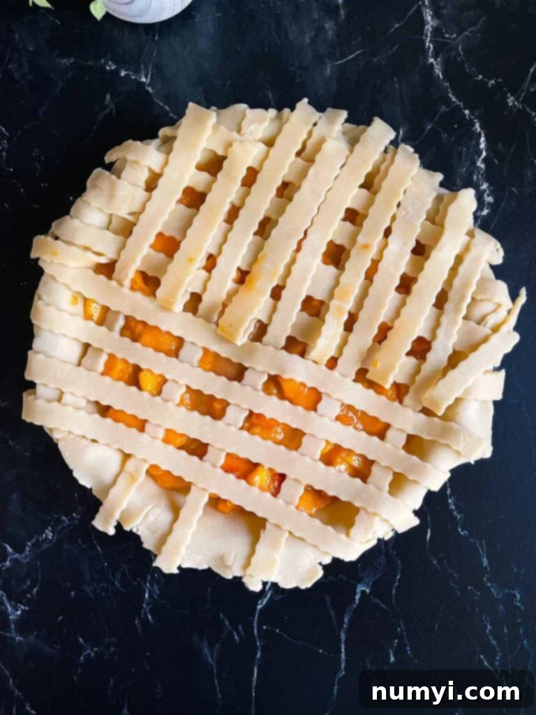 A homemade peach pie with a lattice crust in progress, showing the weaving technique.