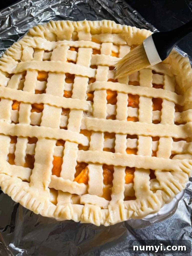 A pastry brush applying a golden egg wash to a meticulously woven lattice pie crust before baking.