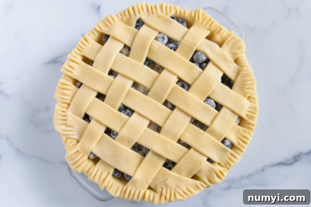 Unbaked blueberry pie with a lattice crust on a light surface.