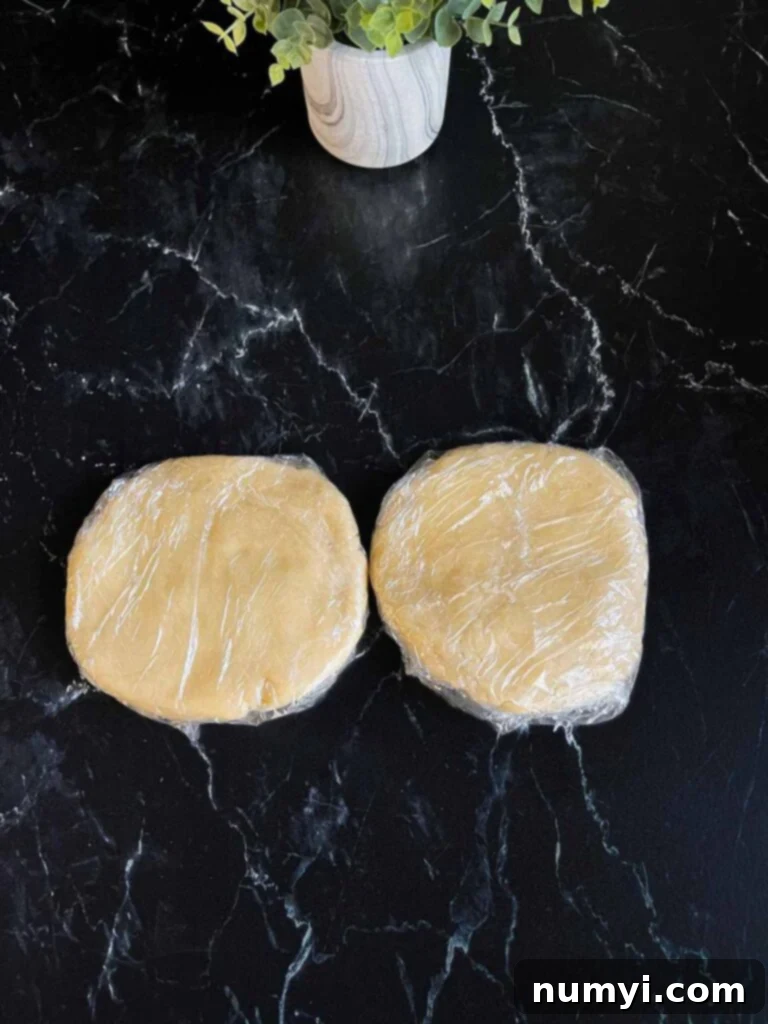 Pie crust dough wrapped in plastic wrap on a dark surface.