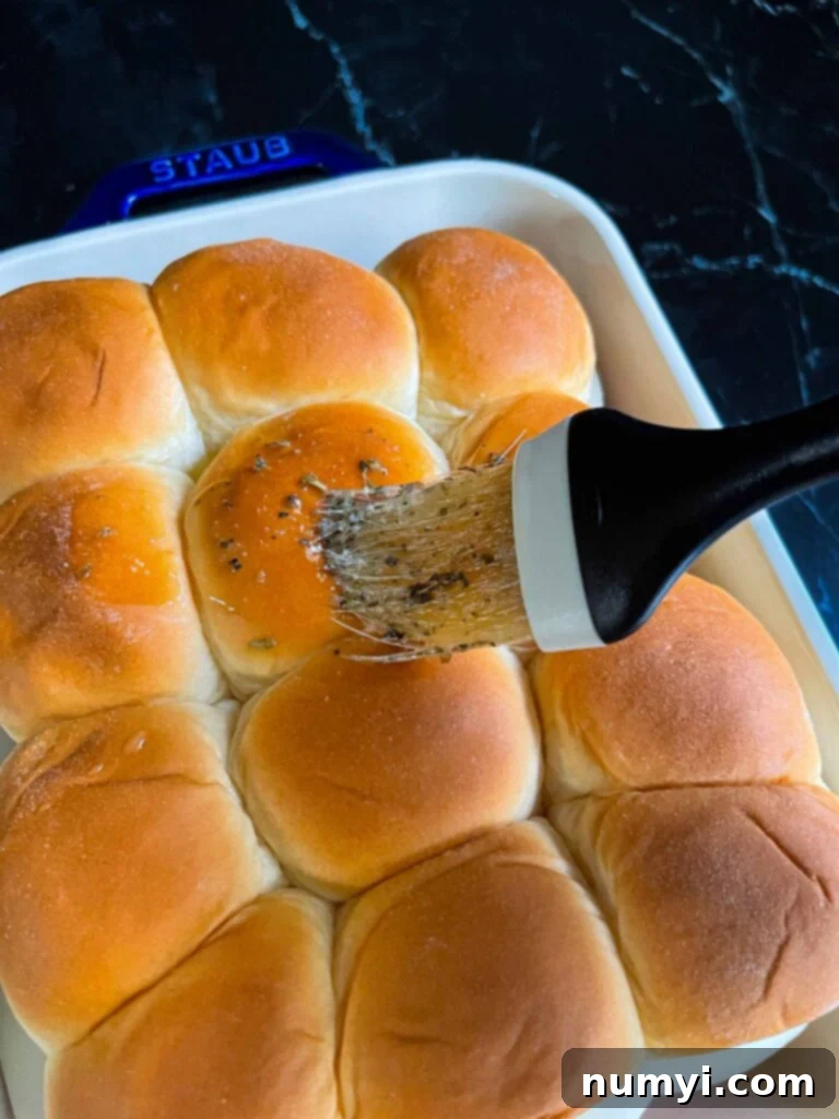 Brushing the tops of the chicken parmesan sliders with the herb butter mixture.