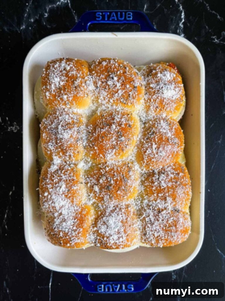 Chicken parmesan sliders topped with grated parmesan cheese in a 9x13 inch baking dish, ready to bake.