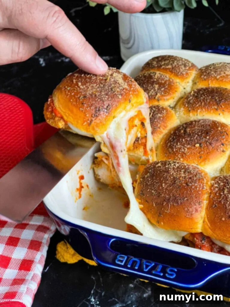 A single chicken parmesan slider being carefully removed from the baking dish with a spatula.
