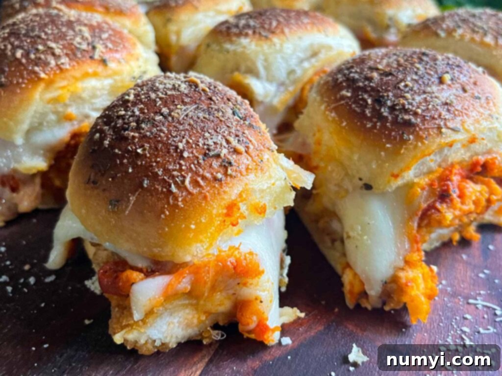 Chicken parmesan sliders arranged artfully on a wooden cutting board, garnished with fresh herbs.