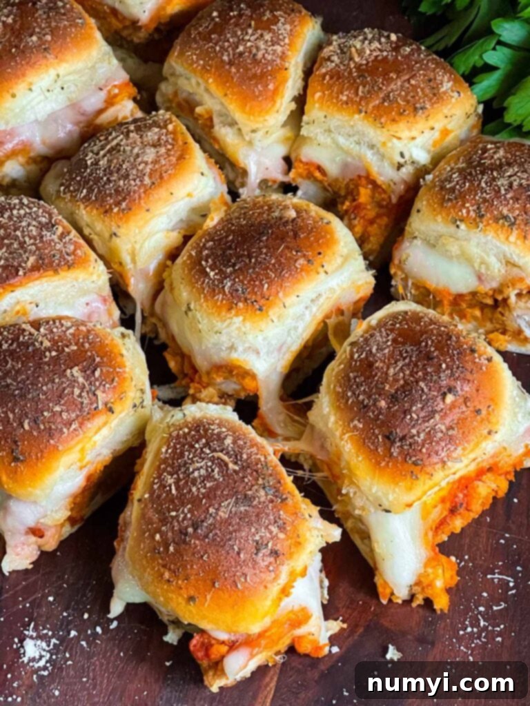 Close-up of baked chicken parmesan sliders on a wooden cutting board, showing melted cheese and golden tops.