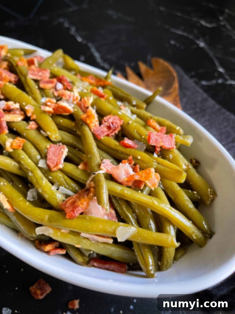 Slow cooker green beans in a white serving bowl on a dark surface.