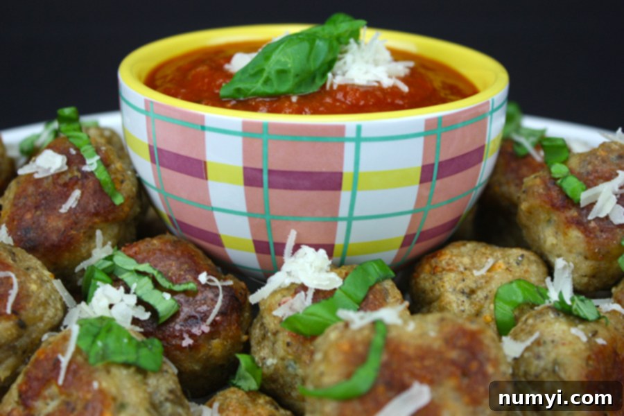 Chicken parmesan meatballs garnished with shredded cheese and basil.