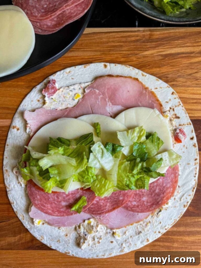 A generous layer of fresh chopped lettuce added as the final filling layer to the Italian pinwheel wrap.
