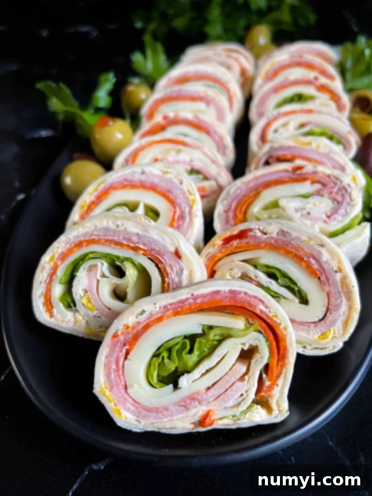 Close-up of Italian pinwheels on a dark plate, showcasing the layers of meat, cheese, and cream cheese spread.