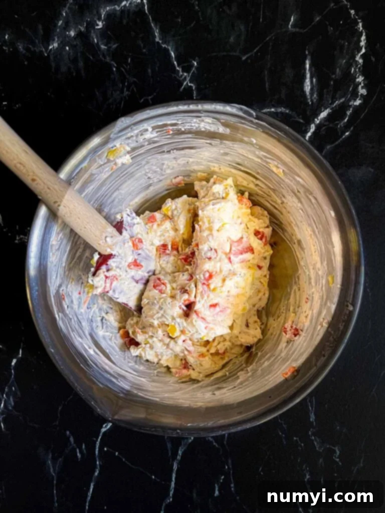 Ingredients for a cream cheese mixture for italian pinwheels mixed together in a silver mixing bowl on a dark surface, after mixing.
