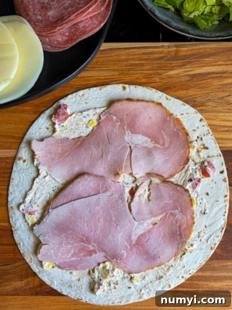 A layer of thinly sliced ham being placed on the cream cheese spread of an Italian pinwheel.