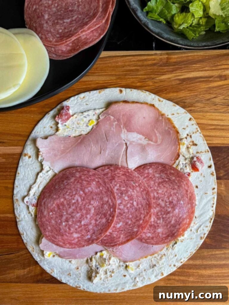 A layer of salami slices being placed over the ham on the Italian pinwheel, ensuring full coverage.