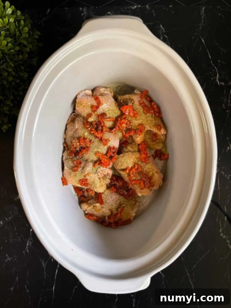 Creamy Slow Cooker Tuscan Chicken 4 Raw chicken and sun-dried tomatoes in a slow cooker for Tuscan chicken.