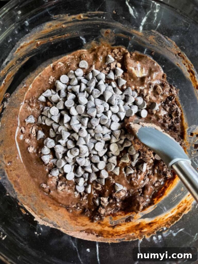 Adding the chocolate chips top the ingredients for double chocolate muffins in a large glass bowl.